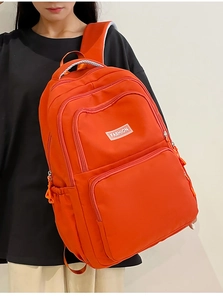 Detail of bright orange nylon backpack with multi-pocket design and fashion logo label