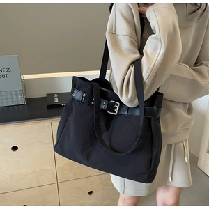 Detail of black fabric tote bag with leather belt strap and metallic eyelets on model