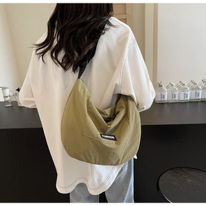 Detail of army green nylon crescent crossbody bag worn by a model in a minimal setting