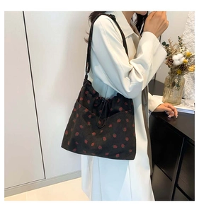 Detail of strawberry print corduroy crossbody bag with drawstring closure and black strap