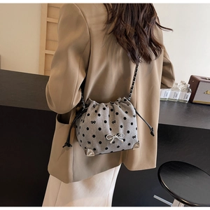 Polka dot canvas bucket bag with metal bow charm shown on a female model's shoulder
