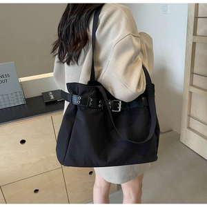 Close-up of black canvas tote bag featuring silver metal buckle and industrial belt detail