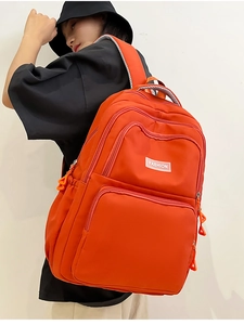 Detail view of bright orange nylon backpack with multi-layer pockets and fashion tag