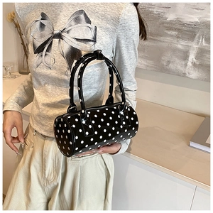 Detail of a black PU leather cylinder bag with white polka dots and silver zipper