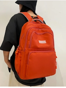 Detail view of water-resistant nylon backpack showing orange multi-pocket zippers and fabric tag