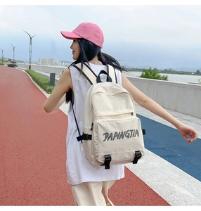 Detailed view of beige nylon backpack featuring front zip pocket and gray logo print