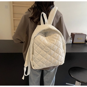 Detail eines weißen gesteppten Rucksacks mit Rautenmuster und Metallreißverschluss