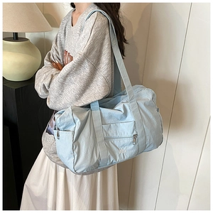 Detail view of light blue nylon shoulder bag featuring exterior zip pocket and VELLA logo