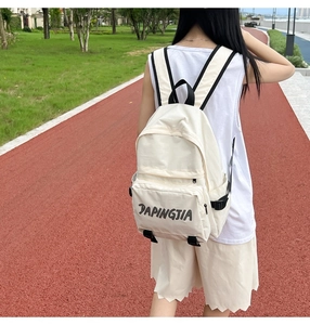Outdoor detail of a minimalist nylon backpack showing the front pocket and logo strap