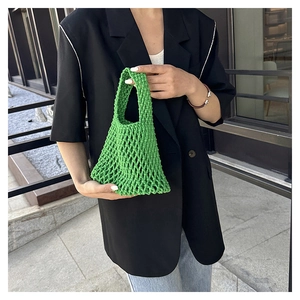 Detail of bright green hand-woven hollow net tote bag held by a model in casual outfit