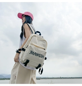 Outdoor shot of cream nylon backpack featuring black buckles and letter print detail
