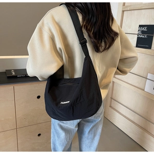 Detail view of black nylon crescent crossbody bag with white fashion logo patch and wide strap