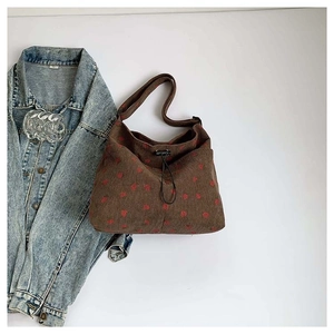Brown corduroy crossbody bag with red heart pattern next to a denim jacket