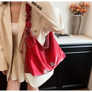 Detail of red patent leather hobo bag featuring pleated shoulder strap and metallic logo