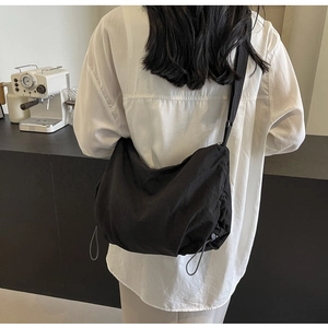 Detail of a large black nylon crossbody bag with textured pleats on a white shirt