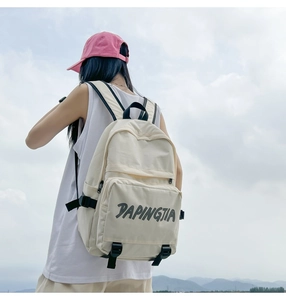 Outdoor shot of a cream white nylon backpack with black zippers and adjustable buckles