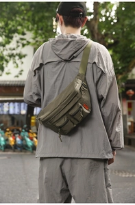 Outdoor shot of army green nylon waist bag featuring multiple pockets and wide strap