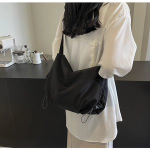 Close-up of a black nylon crossbody bag featuring drawstring details and a wide strap