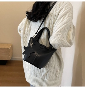 Détail du sac seau noir en similicuir avec pendentif étoile sur un pull blanc tricoté