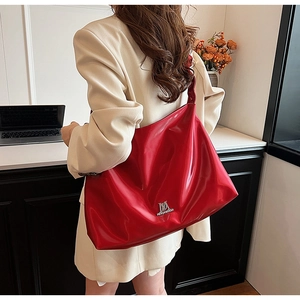 Detail of red glossy PU leather hobo bag with silver metal M logo worn by model
