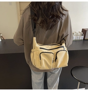 Detail of light beige canvas crossbody bag with multiple zip pockets and black strap