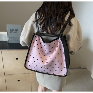 Detail of pink polka dot handbag with metal bow accessory and black trim on model