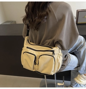 Detail view of a beige canvas crossbody bag featuring functional multi-zipper pockets