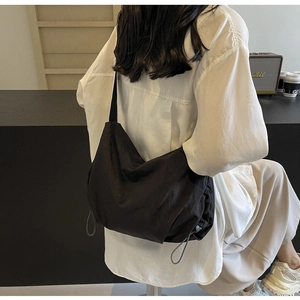 Side view of a large black nylon crossbody bag with drawstring details on model