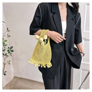 Close-up of yellow woven tote bag with fringe details held by a model in a black blazer