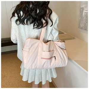 Rear view of a model carrying a light pink nylon shoulder bag with side pockets and zippers