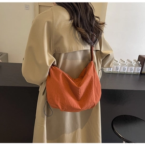 Close-up of a burnt orange crescent hobo bag in textured fabric on female model