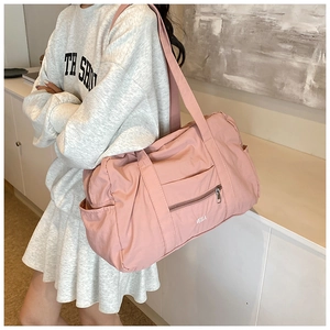 Pink nylon travel tote bag with Velia logo shown on shoulder in a lifestyle setting
