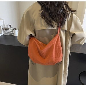 Detailed view of a large orange nylon crossbody bag shown in a lifestyle street style