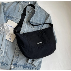 Minimalist black nylon half-moon crossbody bag for women on denim jacket background