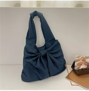 Détail du sac à main en denim bleu foncé avec un grand nœud décoratif et une large bandoulière