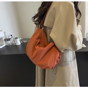 Minimalist burnt orange nylon crescent crossbody bag worn by a model in a cozy cafe setting