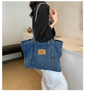 Detail of blue denim tote bag featuring a leather brand tag and striped shoulder strap