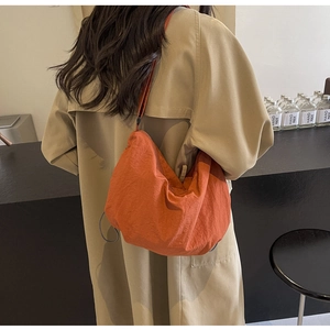 Detail of a vibrant orange nylon crossbody bag with textured fabric on a female model