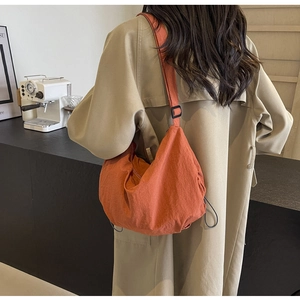 Detail of orange drawstring crossbody bag with pleated fabric on khaki coat model