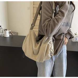 Detail of adjustable black strap and drawstring on beige nylon crescent crossbody bag