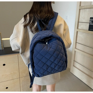 Dunkelblauer gesteppter Nylon-Rucksack mit Rautenmuster, getragen von einem Modell im Raum