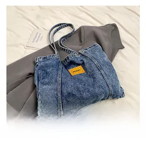 Detail of denim tote bag showing orange leather patch and reinforced handles on blue fabric