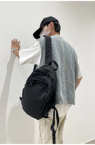 Side view of a minimalist black washed fabric backpack worn by a model on white background