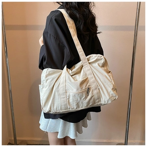 Detail of a large cream nylon tote bag with wide straps and elegant letter embroidery
