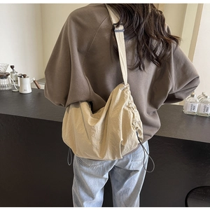 Detail view of the side drawstring and buckle on a beige nylon crossbody bag