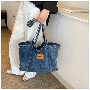 Detailed close-up of large denim tote bag featuring a leather logo patch and sturdy handles