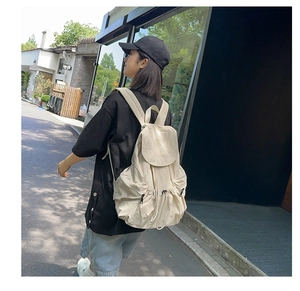 Detail view of large cream nylon backpack with multiple functional zip pockets on street
