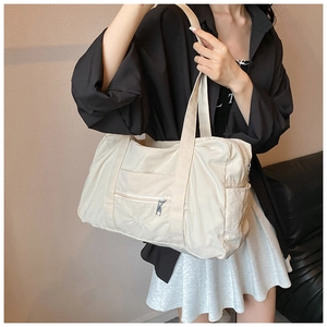 Detail of off-white nylon tote bag showing brand embroidery and front zipper pocket