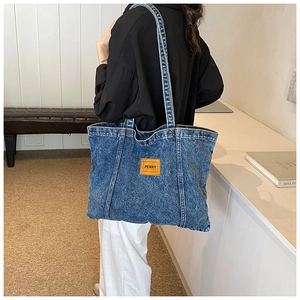 Lifestyle shot of large blue denim tote bag with brown leather patch on shoulder