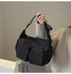 Detail of a casual black nylon crossbody bag with dual front pockets held by a model